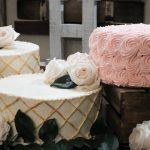 2 white wedding cakes with gold lattice and white roses next to a pink rosette buttercream cake