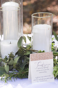 White pillar candles in clear cylinder vases on a white table cloth with greenery wedding centerpiece