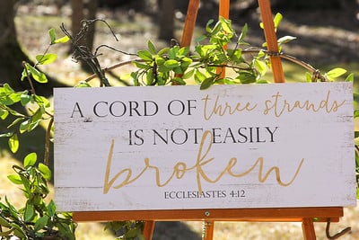 White Bible verse sign, "A cord o three strands is not easily broken" on an easel for a wedding