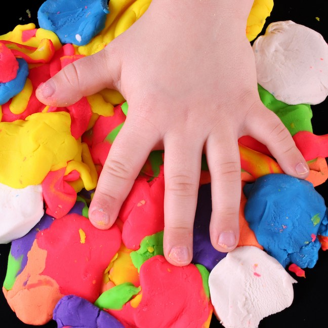 child's hand over colorful clay